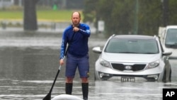 FILE - A man paddles on a stand-up paddle board through a flooded street at Windsor on the outskirts of Sydney, Australia.