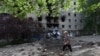 A woman walks past a shell crater in front of a damaged residential building in the town of Siversk, Donetsk region, on June 23, 2022, amid Russia's military invasion launched on Ukraine.