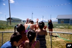 Tyisha ArrowTop Knot, right, sprays her nieces and nephews with a garden hose while looking after them in the backyard of their home on the Blackfeet Indian Reservation in Browning, Mont., Thursday, July 12, 2018. (AP Photo/David Goldman)