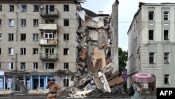 Un residente local pasa junto a un rescatista ucraniano que trabaja fuera de un edificio parcialmente destruido después de un ataque con misiles rusos en Kharkiv el 11 de julio de 2022.