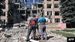 Workers stand outside a partially destroyed educational and laboratory building of a college hit the day before by a rocket in Kharkiv on June 21, 2022. 