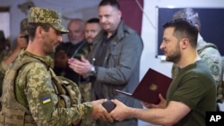 Presiden Ukraina Volodymyr Zelenskyy, kanan, memberikan penghargaan kepada seorang prajurit saat ia mengunjungi wilayah Mykolaiv yang dilanda perang. (Foto: via AP)