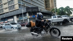 Un hombre levanta los pies mientras conduce una motocicleta para evitar mojarse después de las lluvias causadas por el potencial ciclón tropical dos, en Caracas, Venezuela, el 29 de junio. , 2022. REUTERS/Leonardo Fernández Viloria