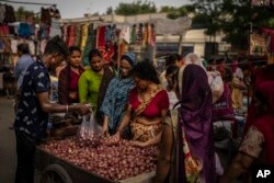 Seorang pedagang pinggir jalan mengemas bawang bombay dalam kantong plastik saat wanita berbelanja di pasar mingguan di New Delhi, India, Rabu, 29 Juni 2022. (AP/Altaf Qadri)