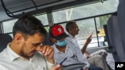 Indian journalist Mohammed Zubair, center, wearing a cap and a face mask, sits in a police vehicle in New Delhi, June 28, 2022.