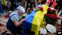 A woman kneels at activist and soldier Roman Ratushnyi's coffin during his memorial service in Kyiv, Ukraine, June 18, 2022. Ratushnyi died in a battle near Izyum, where Russian and Ukrainian troops are fighting for control of the area. 