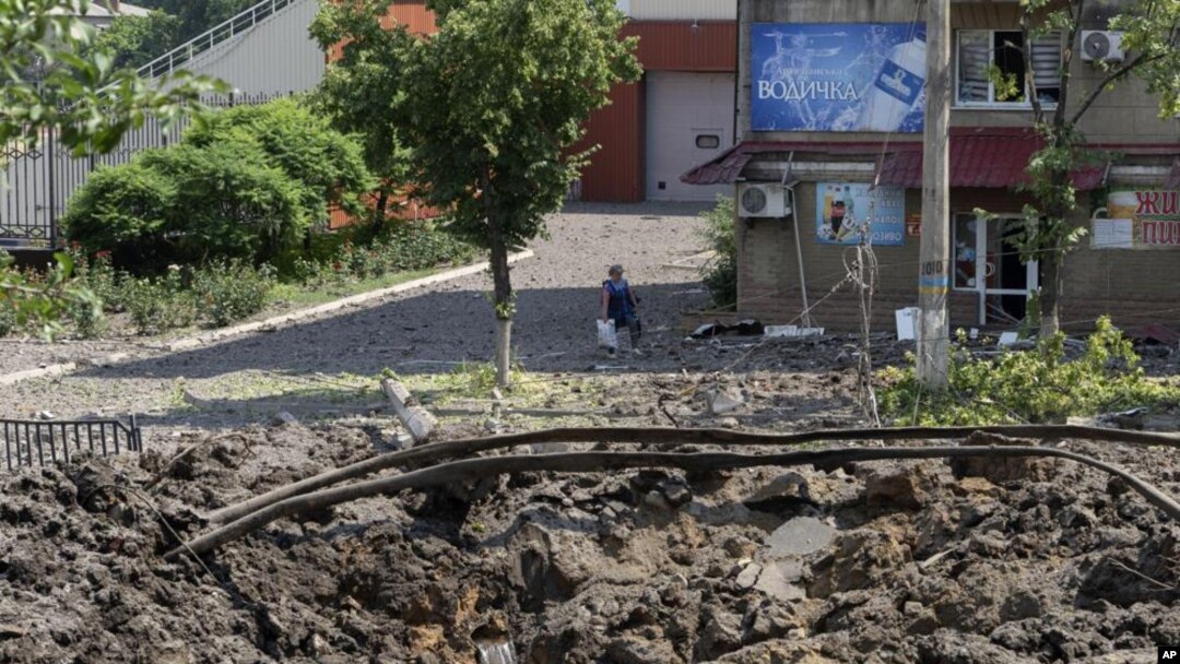 Una mujer camina al lado de un enorme cráter causado por un ataque ruso con misiles en el centro de la ciudad de Bakhmut, Donetsk., el viernes 1 de julio de 2022. (AP Foto/Efrem Lukatsky)