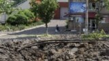 Una mujer camina al lado de un enorme cráter causado por un ataque ruso con misiles en el centro de la ciudad de Bakhmut, Donetsk., el viernes 1 de julio de 2022. (AP Foto/Efrem Lukatsky)