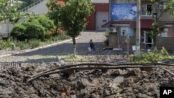 Una mujer camina al lado de un enorme cráter causado por un ataque ruso con misiles en el centro de la ciudad de Bakhmut, Donetsk., el viernes 1 de julio de 2022. (AP Foto/Efrem Lukatsky)