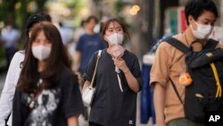 A woman uses a portable electric fan while strolling down the street with her friends in Tokyo, June 27, 2022. 