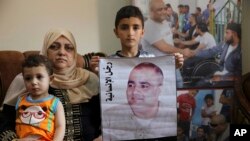 Amal el-Halabi duduk bersama kedua cucunya, di mana salah satunya memegang poster berisi wajah ayahnya Mohammed el-Halabi, yang ditahan oleh pihak keamanan Israel. Foto diambil di rumah Amal di Jalur Gaza, pada 8 Agustus 2016. (Foto: AP/Adel Hana)