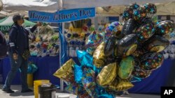 A ballon street vendor adjusts a 'Happy Father's Day' sign in Los Angeles on Saturday, June 18, 2022. 