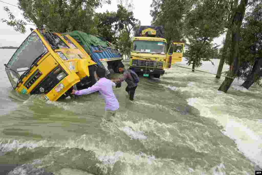 People wade past stranded trucks on a flooded street in Sunamganj, Bangladesh.