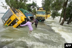 孟加拉國兩名男子設法渡過一條洪水衝擊的街道。（2022年6月21日）