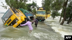 People wade past stranded trucks on a flooded street in Sunamganj, Bangladesh, June 21, 2022.