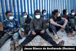 Migran duduk di luar pusat migran sementara saat melintasi pagar perbatasan di kantong Melilla, Spanyol, Afrika Utara, Spanyol 19 Januari 2021. (REUTERS/Jesus Blasco de Avellaneda)