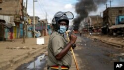 FILE - A police officer holds a pistol during clashes with protesters near a burning tire barricade in the Kariobangi slum of Nairobi, Kenya. Taken 5.8.2020