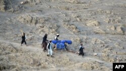 FILE - Volunteers carry aid being received from the International Organization for Migration (IOM) for recent earthquake affected people in the Afghan-Dubai village of Spera district in Khost province, June 26, 2022. 