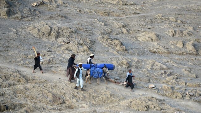 FILE - Volunteers carry aid being received from the International Organization for Migration (IOM) for recent earthquake affected people in the Afghan-Dubai village of Spera district in Khost province, June 26, 2022.