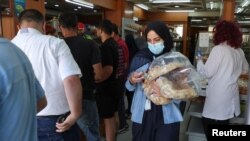 People queue as a woman carries several loafs of bread at a bakery in Beirut, Lebanon, June 29, 2022.
