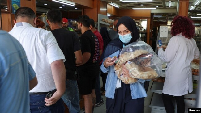 People queue as a woman carries several loafs of bread at a bakery in Beirut, Lebanon, June 29, 2022.