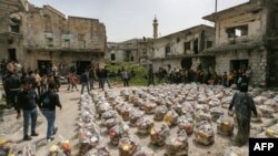 FILE - Locals arrive to receive humanitarian food aid packages being handed over by a volunteer team of first responders in the town of al-Najieh in the western countryside of Syria's rebel-held northwestern Idlib province on April 6, 2022.