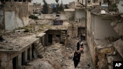 FILE - Women walk in a neighborhood heavily damaged by airstrikes in Idlib, Syria, March 12, 2020. 