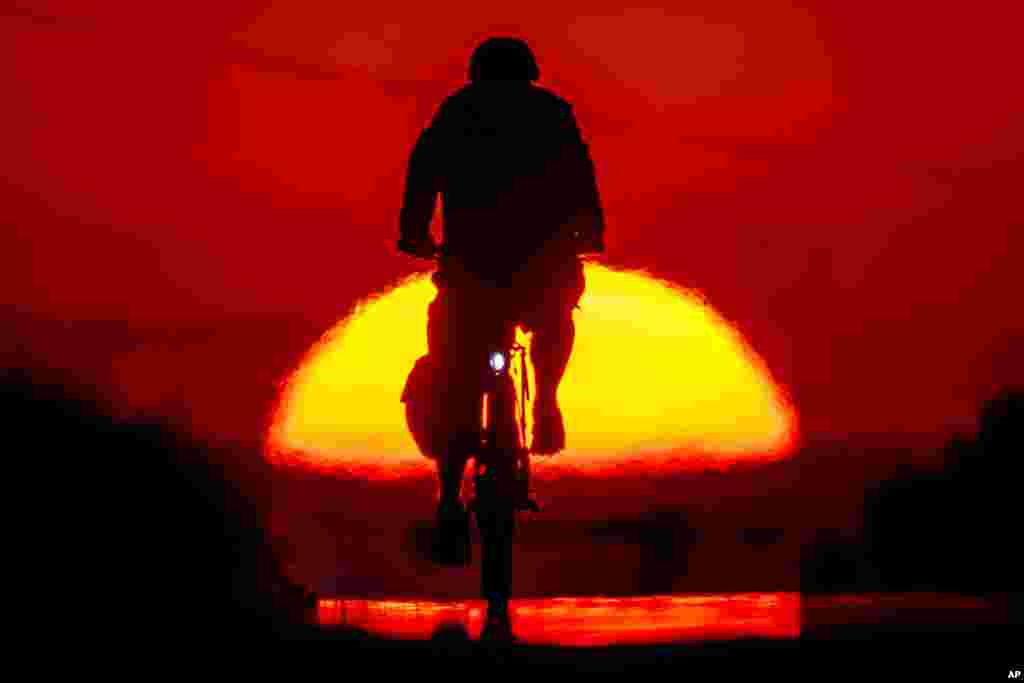 A man rides his bike to work on a small road as the sun rises on the outskirts of Frankfurt, Germany.