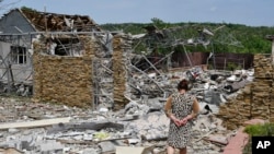 FILE - An elderly woman walks next to a building damaged by an overnight missile strike in Slovyansk, Ukraine, Wednesday, June 1, 2022.
