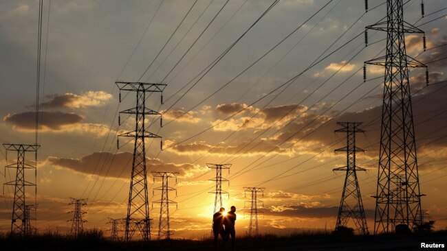 FILE - Locals walk past electricity pylons during frequent power outages from South African utility Eskom, in Soweto, South Africa, April 4, 2022.
