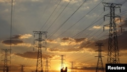 FILE - Locals walk past electricity pylons during frequent power outages from South African utility Eskom, in Soweto, South Africa, April 4, 2022.