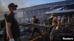 Para petugas penyelamat tampak membereskan puing-puing di lokasi pusat perbelanjaan yang terkena serangan rudal Rusia di Kremenchuk, Poltava, Ukraina, pada 7 Juni 2022. (Foto: Reuters/Anna Voitenko)