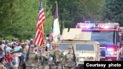Lima tentara yang memegang bendera AS dan memanggul senjata, berpawai di depan sebuah kendaraan militer dan sebuah truk pemadam kebakaran, disaksikan puluhan orang di sebuah jalan di kota Happy Valley, negara bagian Oregon (foto: dok).