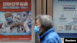 FILE - A person walks past a poster encouraging elderly people to get vaccinated against COVID-19, near a residential compound in Beijing, China, March 30, 2022. 