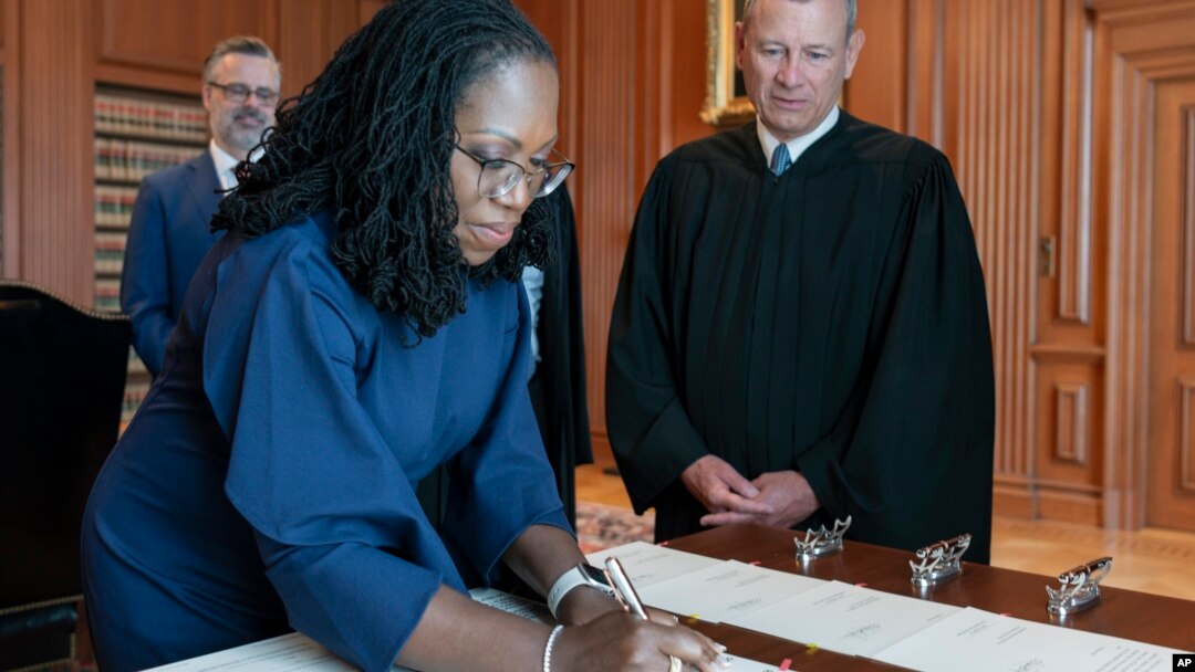 In this image provided by the Collection of the Supreme Court of the U.S., Supreme Court Justice Ketanji Brown Jackson signs the Oaths of Office at the Supreme Court in Washington, June 30, 2022, as Chief Justice of the United States John Roberts watches.