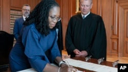 In this image provided by the Collection of the Supreme Court of the U.S., Supreme Court Justice Ketanji Brown Jackson signs the Oaths of Office at the Supreme Court in Washington, June 30, 2022, as Chief Justice of the United States John Roberts watches.