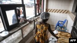 Un employé d'une boulangerie vend du pain à base de farine de blé et de manioc à des clients à Yopougon, un quartier populaire d'Abidjan le 26 juin 2022.