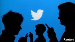 FILE - People holding mobile phones are silhouetted against a backdrop projected with the Twitter logo in this illustration picture taken Sept. 27, 2013. 