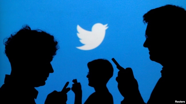 FILE - People holding mobile phones are silhouetted against a backdrop projected with the Twitter logo in this illustration made Sept. 27, 2013.