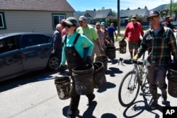 An ad-hoc "bucket brigade" of volunteer cleanup workers walk down a street in Red Lodge, Mont. as they head to a flood-damaged house to remove mud and water from its basement, June 16, 2022.