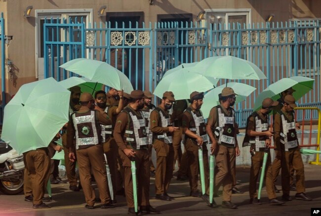 Saudi traffic policemen raise umbrellas at the Mina tent camp, in the Saudi Arabia's holy city of Mecca, Tuesday, July 5, 2022. Saudi Arabia is expected to receive one million Muslims to attend Hajj pilgrimage, which will begin on July 7, after two years of limiting the numbers because coronavirus pandemic. (AP Photo/Amr Nabil)