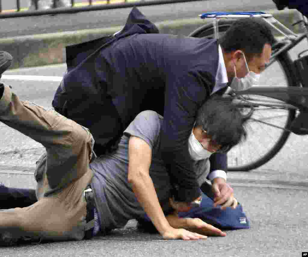 Tetsuya Yamagami, bottom, is detained near the site of gunshots in Nara Prefecture, western Japan. Former Japanese Prime Minister Shinzo Abe died after being shot during a campaign speech.