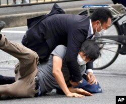 Tetsuya Yamagami, bottom, is detained near the site of gunshots in Nara Prefecture, western Japan. Former Japanese Prime Minister Shinzo Abe died after being shot during a campaign speech.