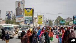 FILE: Somalis walk past billboards showing candidates Abdirahman Abdishakur Warsame and Omar Abdulkadir Ahmedfiqi in Mogadishu, Somalia, Jan. 29, 2021.