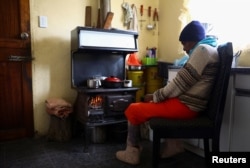 Pinkie Sebitlo warms herself near a coal stove during frequent power outages from South African utility Eskom, in Soweto, South Africa, June 23, 2022.