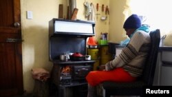 Pinkie Sebitlo, habitante de Soweto, se réchauffe près d'un poêle à charbon pendant une panne de courant, le 23 juin 2022.