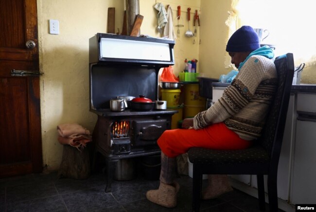 Pinkie Sebitlo warms herself near a coal stove during frequent power outages from South African utility Eskom, in Soweto, South Africa, June 23, 2022.