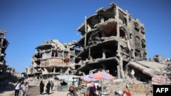 FILE - A man cycles past vendors offering goods for sale outside heavily damaged buildings in a camp sheltering people displaced by the Israel-Hamas conflict, in Jabalia in the northern Gaza Strip, Sept. 8, 2024.