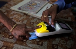 FILE - An impoverished woman places her finger on a biometric card reader before buying her quota of subsidized rice from a fair price shop under the Public Distribution System in Rayagada, India.