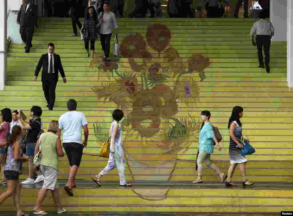 People walk on stairs featuring a five-meter-high reproduction of Vincent van Gogh&#39;s signature painting &quot;Sunflowers&quot,; at the entrance to Ocean Terminal in Hong Kong.